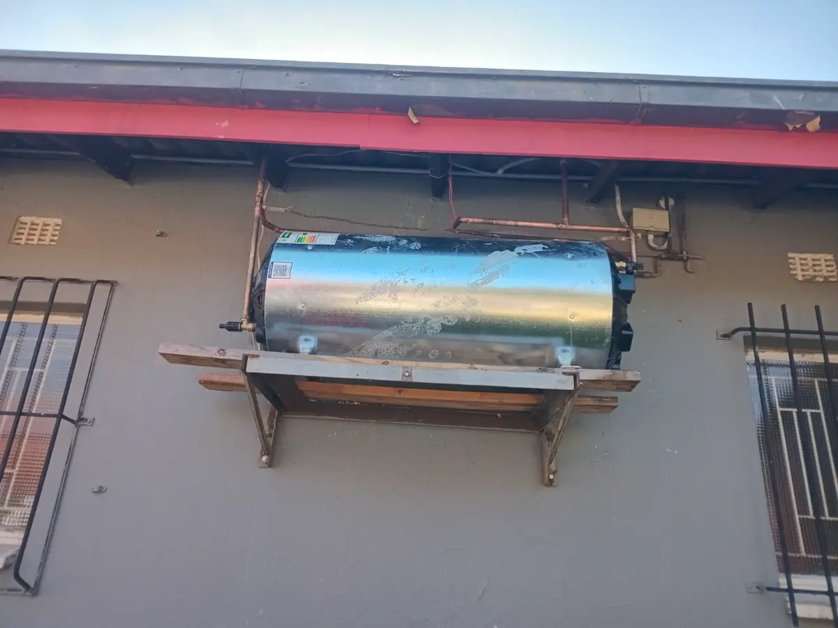 Weathered cylindrical solar water heater mounted against an exterior wall